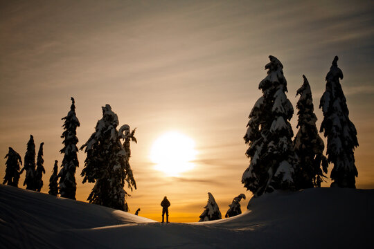 Person silhouetted on snowy mountain at sunset