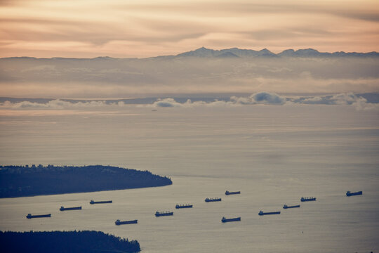Cargo ships wait in a hazy ocean bay at sunset