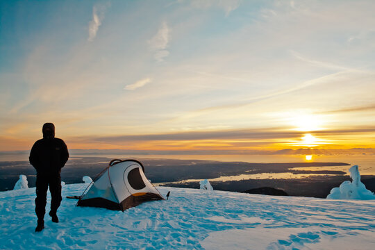 Man camping on snowy peak at sunset