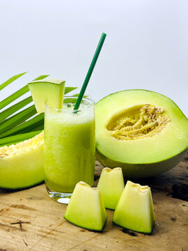 Refreshing homemade honeydew melon juice served in a glass with fresh melon wedges and ripe green melon on a rustic wooden table. Healthy organic fruit beverage rich in hydration, vitamins, and natura