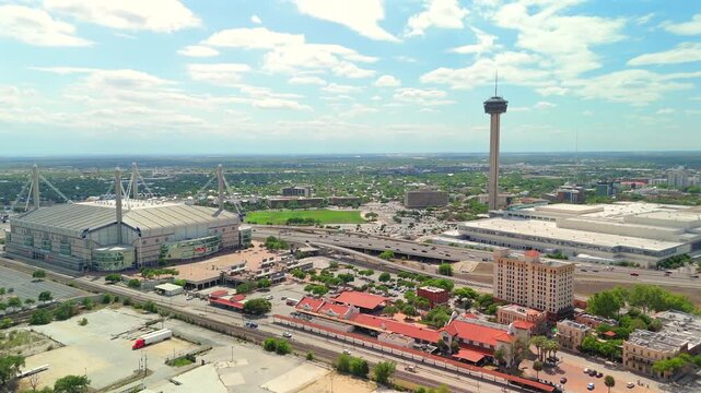 The drone reveals the Alamodome distinctive cable roof structure beside a green sports field.