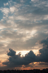 Fototapeta premium A dramatic cloudy sunset sky over a dark city silhouette. Golden sunlight rays breaking through thick clouds create a peaceful atmospheric evening landscape. Perfect for travel backgrounds.