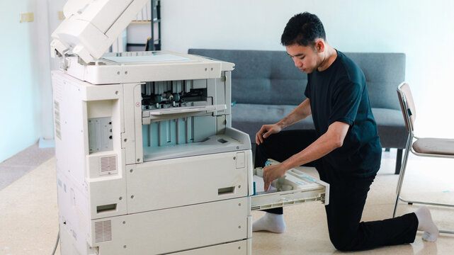 Office technician inspecting an open commercial photocopier while holding printed documents, representing printer repair, maintenance, troubleshooting,