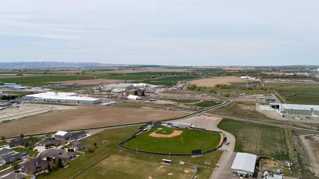 Aerial view of a baseball field surrounded by vacant land near a growing development.