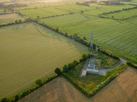 Aerial view of electrical substation and high voltage power lines across agricultural landscape at sunset.Renewable energy infrastructure and power distribution network in a rural landscape.