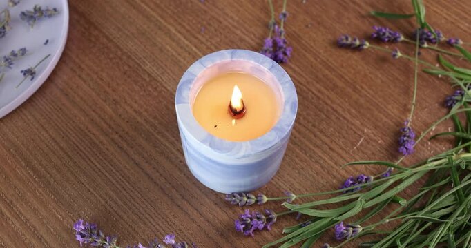 Burning candle lavender background video. Scented wax candle glows on wooden table with fresh purple blossoms. Cozy aromatherapy setup for spa relaxation or wellness mindfulness video footage.