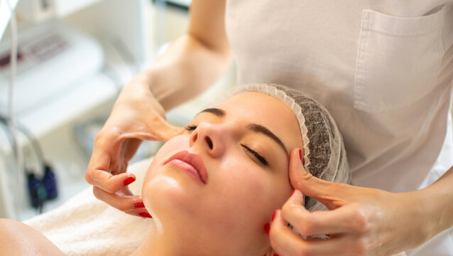 Professional cosmetologist doing relaxing manual facial massage for young woman at spa