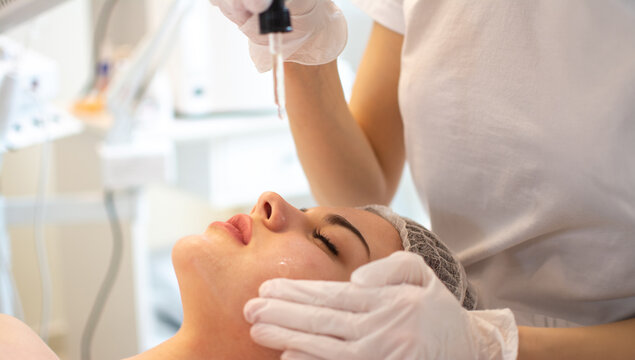 Professional beautician applying vitamin serum from dropper on woman facial skin
