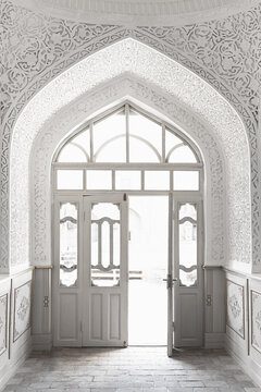 Ornate white pointed arch doorway inside Muhammad Amin Khan Madrasa in Ichan Kala, Khiva. Intricate carved plaster decoration surrounds the entrance, ideal for travel and architectural publications.