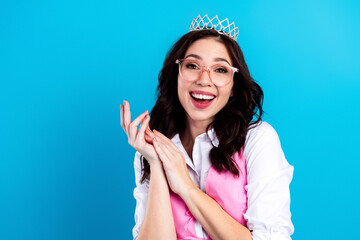 Young woman wearing a tiara and glasses smiling joyfully against a bright blue background celebrating confidence and fun © deagreez