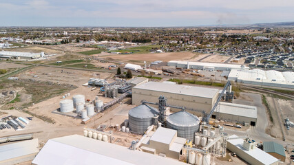 Aerial view of a grain storage facility with silos and a small town visible in the distance. © Moiseii Production