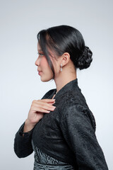 Profile portrait of an elegant Indonesian woman touching her chest in a black lace kebaya. © Saddha Visual