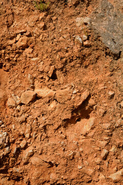 A close up shot of a rough natural terrain featuring red clay bauxite soil mixed with small rocky stones and dry minerals under daylight