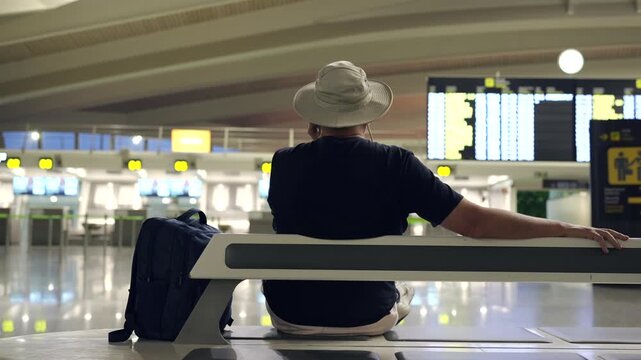 Male traveler waiting on airport bench watching flight board