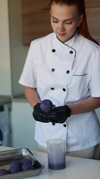 Female pastry chef glazing cake pop with purple chocolate coating
