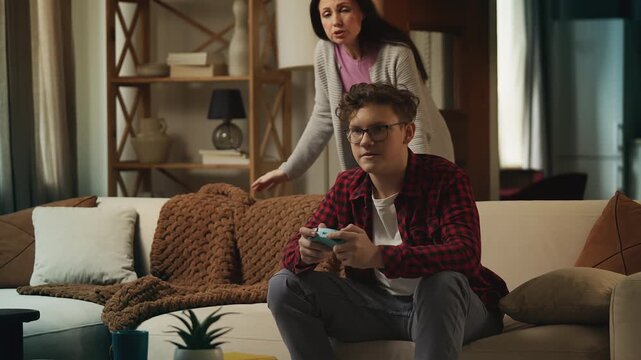 Annoyed mother scolding her teen son for playing video games, rebellious phase