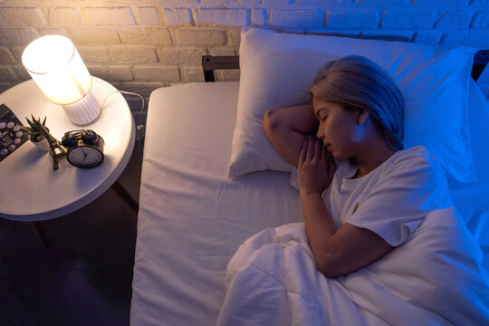 Asian woman sleeps soundly on a soft, silky bed under the nighttime lights in her bedroom.