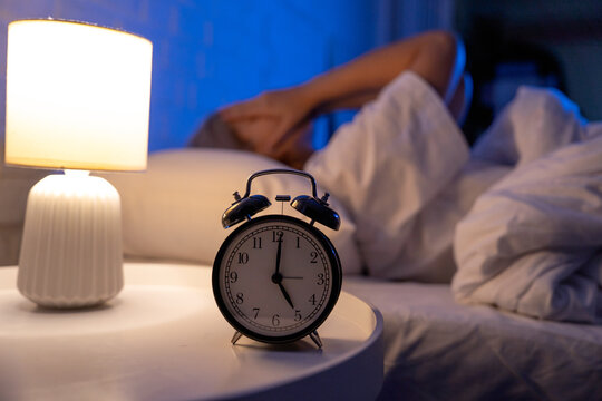 An irritable Asian woman wakes up in the middle of the night. She covers her face with her hands because of the disturbing noise. She can't sleep, restless, confused and agitated.