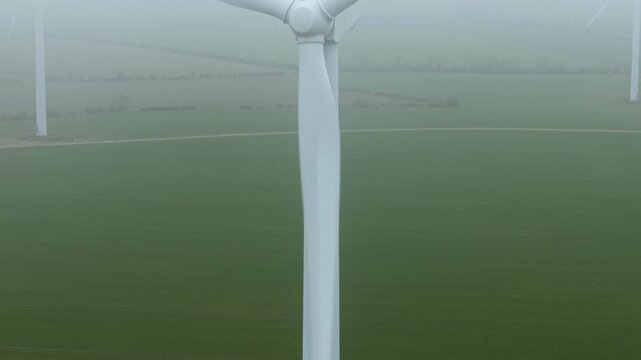 Drone rising above a thick blanket of mist to reveal large eco-friendly wind turbines at Cotton Farm, Cambridgeshire.