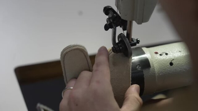Artisan feeding a rolled suede strip through a sewing machine to bind a glove edge