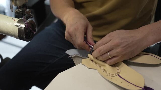 Worker hand assembling a leather glove with a purple accent at the sewing station