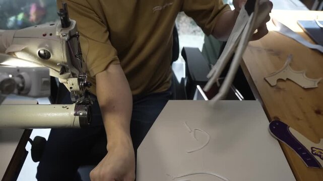 Craftsman sewing assembled baseball glove pieces with purple trim at a sewing station