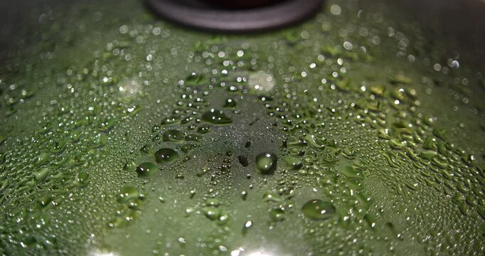Close overhead detail shows clusters of steam droplets merging into irregular trails across a glass lid while green beans cook below with soft reflections and shallow focus