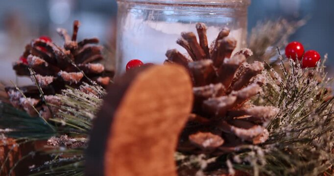 Christmas pinecone and red berry arrangement Macro holiday shot frames a frosted pinecone red berries dried greenery and candle glass behind a softly blurred wooden reindeer ornament