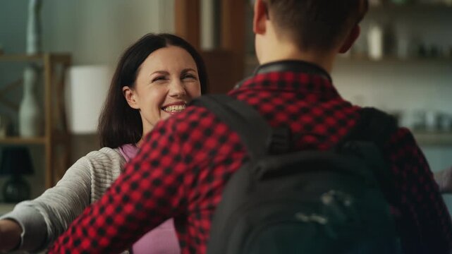 Cheerful middle-aged woman hugging her son returning home from university