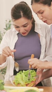 Happy young lesbian couple preparing a healthy fresh vegetable salad together in the modern kitchen.