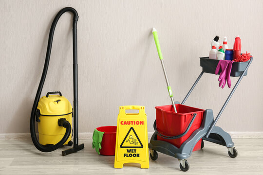 Professional cleaning equipment with a yellow wet floor sign and vacuum cleaner against a light wall, this setup represents comprehensive janitorial services and facility maintenance