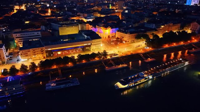 Aerial shot of Bratislava waterfront and Slovak National Gallery. Illuminated ship moving along riverbank near historic building and lit road.