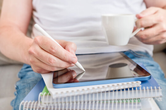 Close-up of student writing notes in digital tablet screen  while sitting on sofa at home, study and education concept for homework, exam preparation, remote learning, planning, productivity