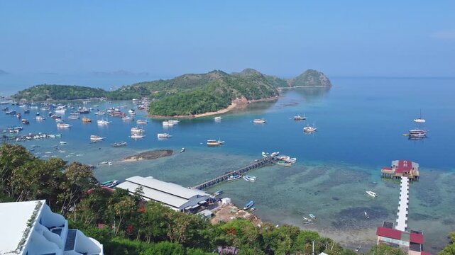 Shutterstock Title / Description
Panoramic aerial view of Labuan Bajo bay filled with anchored boats, wooden jetties, white hillside resort villas, and tropical islands in Indonesia.