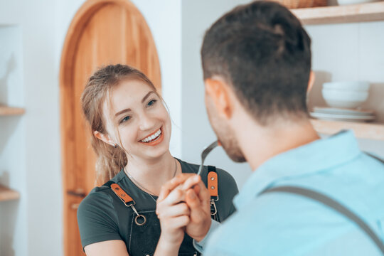Happy couple cooking together in a cozy kitchen, sharing food and smiling. Concept of love, relationship, home lifestyle, and joyful everyday moments in a warm environment