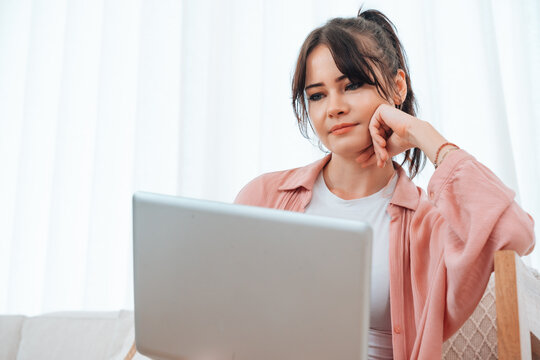 Young caucasian woman relaxing on comfortable couch, using laptop at home, happy female chatting with friends in social network, spending weekend, watching movie, shopping online