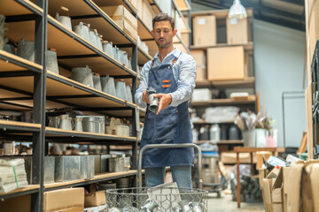 Caucasian male worker in denim apron using barcode scanner on metal bucket in small business...