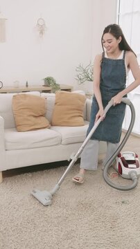 A woman using a canister vacuum cleaner to clean a fluffy carpet in a bright and cozy living room.