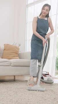 A woman using a canister vacuum cleaner to clean a fluffy carpet in a bright and cozy living room.