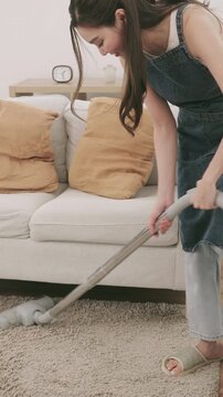 A woman using a canister vacuum cleaner to clean a fluffy carpet in a bright and cozy living room.