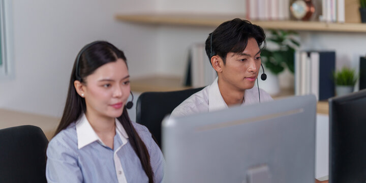 Asian male call center agent wearing headset working at office computer