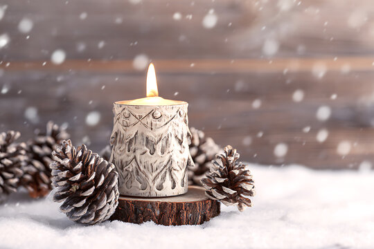 Festive Candle Surrounded by Pine Cones in Snowy Winter Scene.