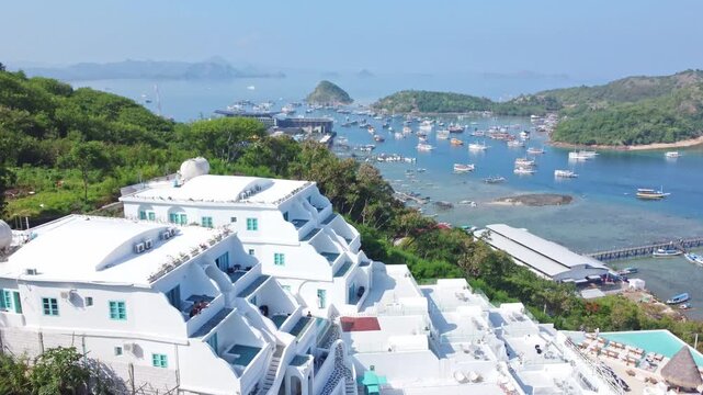 Panoramic aerial view of white hillside resort villas overlooking a harbor filled with boats and tropical islands in Labuan Bajo, Indonesia.