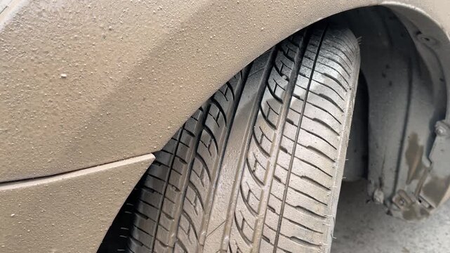 Close view of a muddy tire beneath the wheel arch before washing, revealing thick road grime and dirt accumulation, ideal for vehicle maintenance, detailing and cleaning concepts.