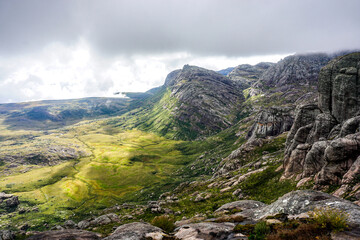 Panoramic view of a rugged mountain valley with rocky cliffs, green meadows, and dramatic storm clouds. Ideal for travel, nature, adventure, sustainability, and outdoor marketing. © Duro Mesiar