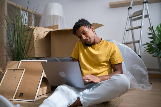 Man multitasking with phone and laptop among moving boxes at home