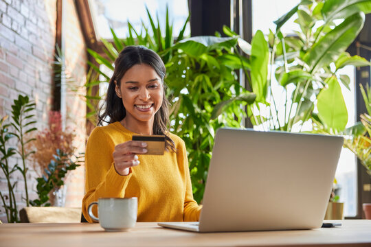 Happy businesswoman looking at credit card by laptop in loft office