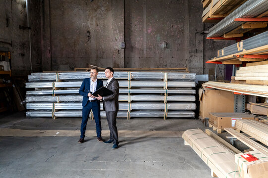 Two businessmen with folder talking in an old storehouse
