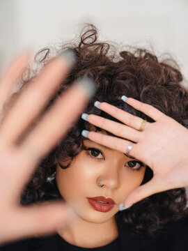 Model framing face with hands indoors