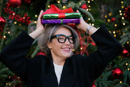 Smiling woman holding Christmas gift on head outdoors during winter